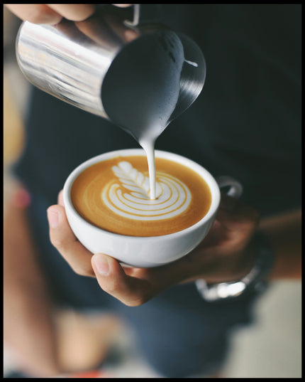 Ein Leinwandbild von einem Barista, der kunstvoll Milch in eine Tasse Kaffee gießt und ein Muster kreiert.