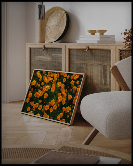 Ein gerahmtes Poster von leuchtend orangefarbenen Blumen in voller Blüte, an einer Holzkommode angelehnt und stehend auf dem Holzboden