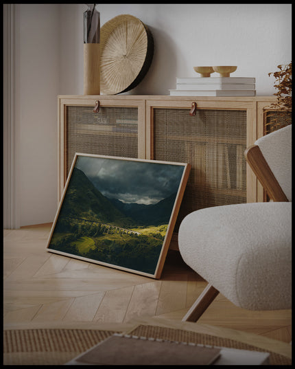 Ein gerahmtes Poster von dem Glenfinnan-Viadukt bei bewölktem Himmel, an einer Holzkommode angelehnt und stehend auf dem Holzboden