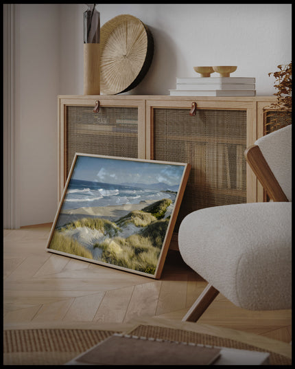 Ein gerahmtes Poster vom Meerblick über Dünen und Strand, an einer Holzkommode angelehnt und stehend auf dem Holzboden