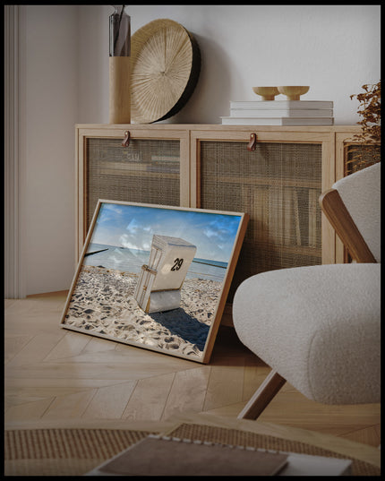 Ein gerahmtes Poster von einem weißen Strandkorb am Strand der in Richtung Meer gerichtet ist, an einer Holzkommode angelehnt und stehend auf dem Holzboden