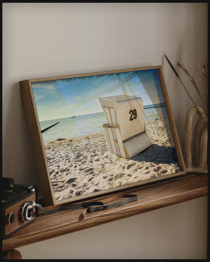 Ein gerahmtes Poster von einem weißen Strandkorb am Strand der in Richtung Meer gerichtet ist, auf einem Holzregal an die Wand angelehnt