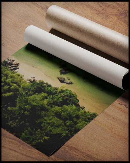 Ein Poster von einem Sandstrand mit grünlichem Wasser vor einem tropischen Wald, gerollt auf einer Holzoberfläche liegend