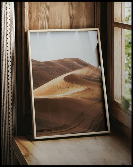 Ein gerahmtes Poster von einer Sanddüne in der Wüste, vor einem Fenster an die Wand angelehnt